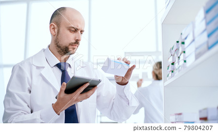 pharmacist with a digital tablet looking at a box of medicines. 79804207
