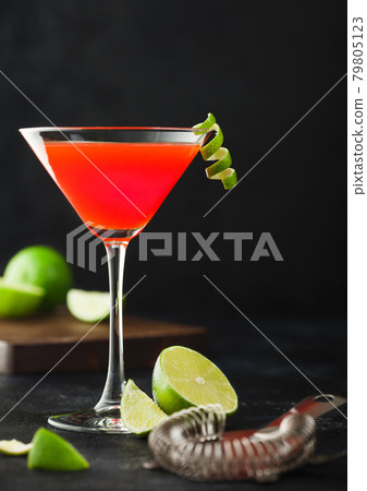 Cosmopolitan cocktail in classic crystal glass with lime peel and fresh limes with strainer 79805123