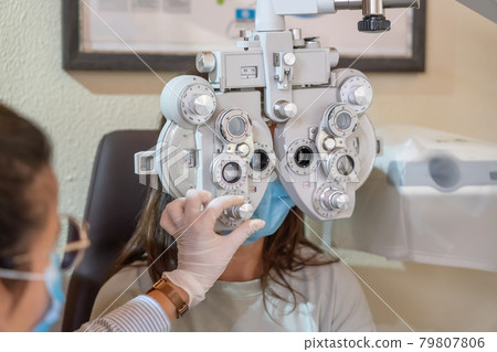 Young girl in mask at the ophthalmologist's appointment. Eyesight check. The ophthalmologist makes a correction. Close-up. 79807806
