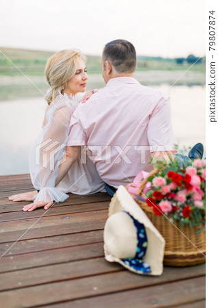 Man and lady, sitting together on the wooden bridge on the shore of lake 79807874