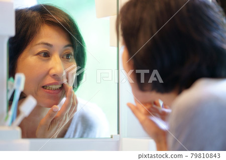 Middle-aged woman looking at her teeth in the mirror 79810843