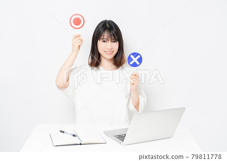 A young woman holding an OK and NG placard while using a laptop in front of a white background 79811778