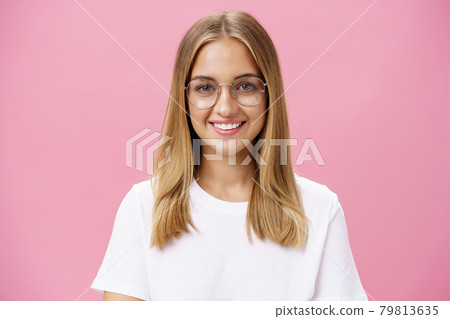 Creative and smart good-looking friendly female with tanned skin and little pimples wearing glasses and white t-shirt smiling broadly with perfect teeth standing plesant over pink wall Creative and smart good-looking friendly female with tanned skin and little pimples wearing glasses and white t-shirt smiling broadly with perfect teeth standing plesant over pink wall 79813635