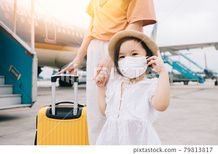 Adorable baby wearing a mask with a yellow suitcase at the airport 79813817