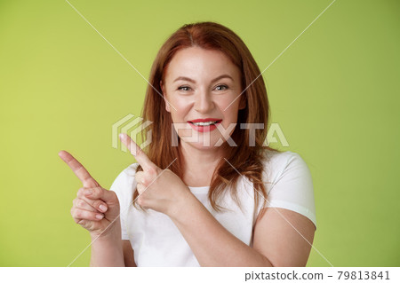 Close-up joyful motivated pleasant redhead middle-aged female pointing upper left corner index fingers smiling delighted give advice check-out promo good advertisement blank space green background 79813841