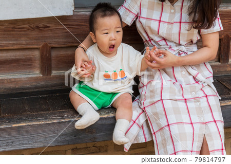A boy having a good time sitting on the porch of a Hanok with his mother 79814797