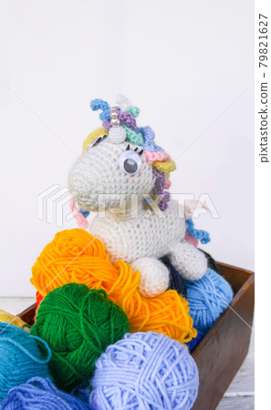 Handmade crocheted unicorn toy and yarn in a wooden box on white background. 79821627