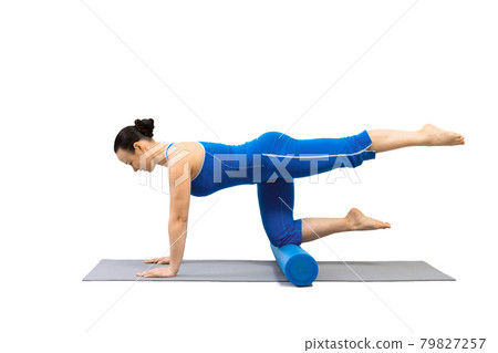 Pilates drill, isolated on white. Adult caucasian woman in blue sportswear practice exercise bird dog with one leg up and foam roller under her knees. Pilates drill, isolated on white. Adult caucasian woman in blue sportswear practice exercise bird dog with one leg up and foam roller under her knees. 79827257