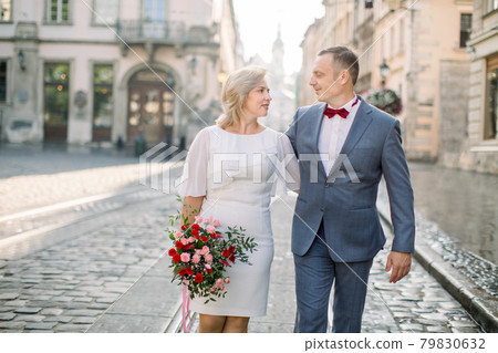 Mature couple in elegant fashionable clothes, walking in the street of old European city Mature couple in elegant fashionable clothes, walking in the street of old European city 79830632