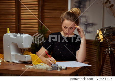 Beautiful young seamstress working on sewing machine Beautiful young seamstress working on sewing machine 79831497