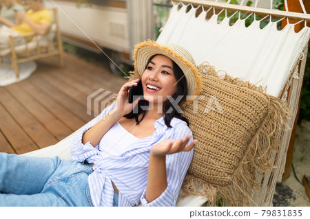 Asian woman lying in hammock near camper van, speaking on smartphone, enjoying summer vacation in countryside Asian woman lying in hammock near camper van, speaking on smartphone, enjoying summer vacation in countryside 79831835