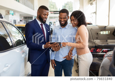 Dealership Center Manager Showing Vehicle Characteristics On Digital Tablet To Black Couple Dealership Center Manager Showing Vehicle Characteristics On Digital Tablet To Black Couple 79831840