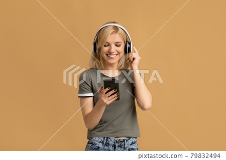 Favorite leisure. Happy millennial woman in wireless headphones listening music online on smartphone Favorite leisure. Happy millennial woman in wireless headphones listening music online on smartphone 79832494