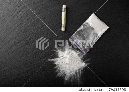Cocaine in a plastic package on a black background, close-up. A rolled up dollar bill for drug use. Cocaine in a plastic package on a black background, close-up. A rolled up dollar bill for drug use. 79833208
