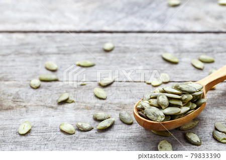 Pumpkin green seeds in a wooden spoon and scattered on a wooden table. 79833390