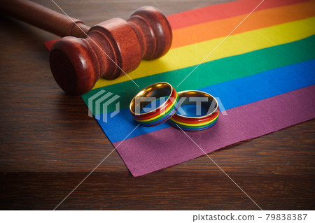 Two gold wedding rings with lgbt rainbow colours. Homosexual marriage. Lgbt rights and law. 79838387