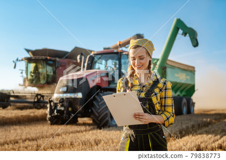 Farmer on grain field with tractor and combine harvester in background 79838773