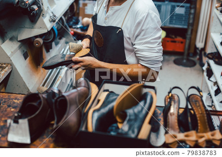 Shoemaker with shoes to repair on a rack in his workshop 79838783