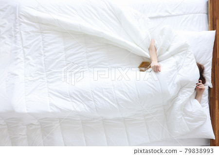 Drunk woman lies with bottle of alcohol in bed closeup 79838993