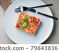 Piece of lasagna. White plate with fork and knife 79843836
