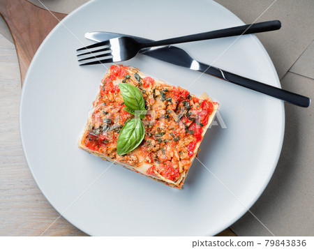 Piece of lasagna. White plate with fork and knife Piece of lasagna. White plate with fork and knife 79843836