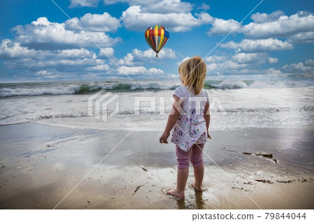 Blond child looking at the sea with blue sky and balloon. Blond child looking at the sea with blue sky and balloon. 79844044