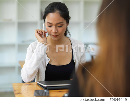 Confident woman looking on tablet while holding stylus pen in front of her friend 79844449