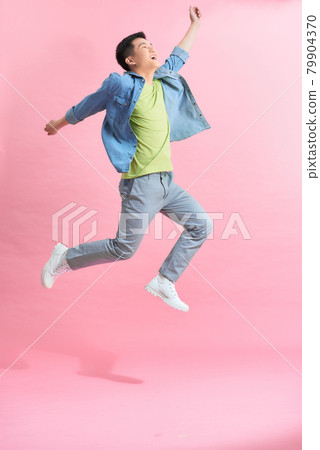 Fun energetic Asian man jumping in mid air isolated on light pink background 79904370