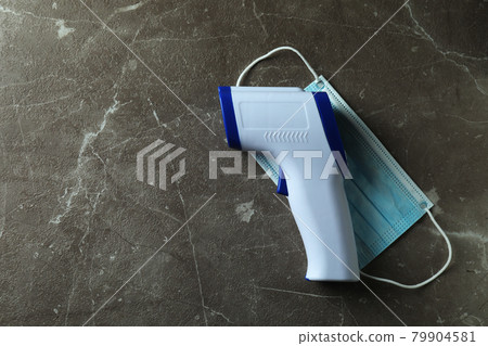 Thermometer gun and medical mask on gray textured background 79904581