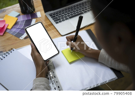 Close up view creative woman using smart phone and writing information on sticky note. Close up view creative woman using smart phone and writing information on sticky note. 79905408