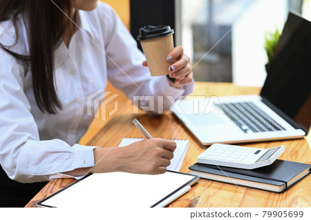 Businesswoman drinking coffee and making note on notebook. Businesswoman drinking coffee and making note on notebook. 79905699