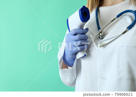 Female doctor hold thermometer gun on mint background Female doctor hold thermometer gun on mint background 79906021