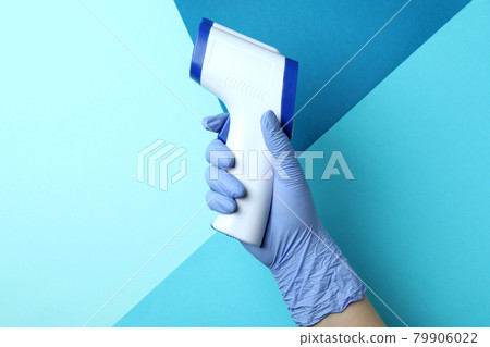 Hand in glove hold thermometer gun on three tone background Hand in glove hold thermometer gun on three tone background 79906022