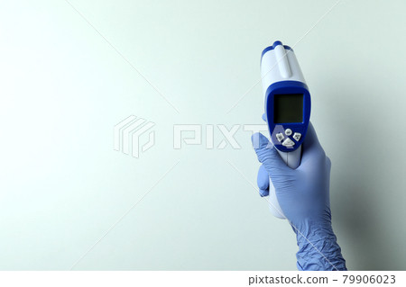 Hand in glove hold thermometer gun on white background Hand in glove hold thermometer gun on white background 79906023