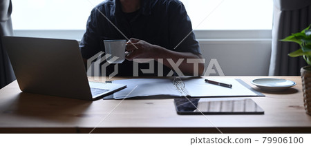 Cropped shot businessman holding coffee cup and checking email on laptop computer. Cropped shot businessman holding coffee cup and checking email on laptop computer. 79906100