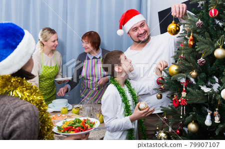 Family decorating Christmas tree and setting table Family decorating Christmas tree and setting table 79907107