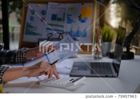A business woman accountant or banker does an audit and calculates expenses for a financial report balance sheet statement using a calculator. The principle of saving and investing. A business woman accountant or banker does an audit and calculates expenses for a financial report balance sheet statement using a calculator. The principle of saving and investing. 79907963
