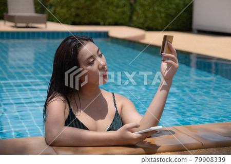 Young woman with bikini in pool using smartphone and holding credit card for shopping online. Everywhere Online shopping concept. Young woman with bikini in pool using smartphone and holding credit card for shopping online. Everywhere Online shopping concept. 79908339