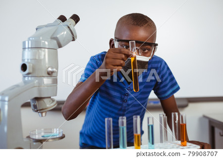 African american schoolboy in safety glasses and face mask looking at test tubes in science class African american schoolboy in safety glasses and face mask looking at test tubes in science class 79908707