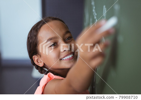 Portrait of mixed race schoolgirl standing writing on chalkboard in classroom Portrait of mixed race schoolgirl standing writing on chalkboard in classroom 79908710