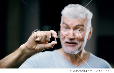 Emotional Handsome gray haired senior man with a pill in his hand. Medicine and health care concept. 79909558