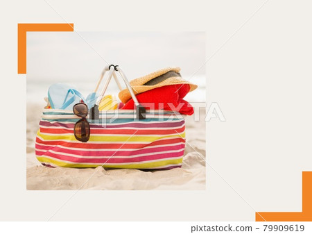 Photograph of bag with accessories at the beach against grey background Photograph of bag with accessories at the beach against grey background 79909619