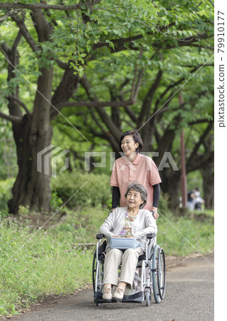 Senior woman and caregiver in a wheelchair taking a walk in the park Senior woman and caregiver in a wheelchair taking a walk in the park 79910177