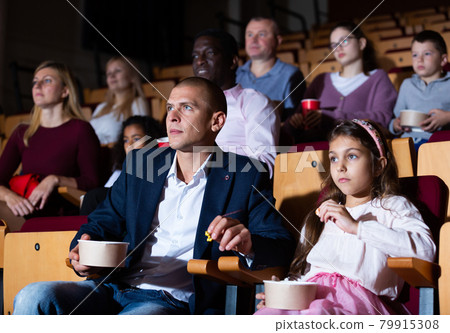 Father and tween daughter watching film together in cinema 79915308