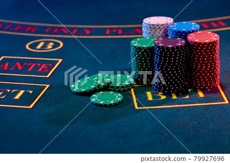 Colorful chips piles, some of them are laying nearby on a blue cover of a playing table. Gambling entertainment, poker, casino concept. Close-up. 79927696