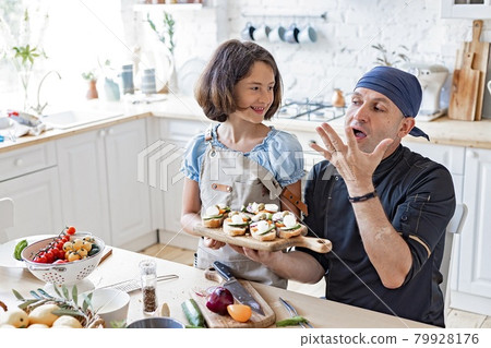 Happy dad chef and his cute daughter are cooking together in the domestic kitchen. Father and daughter are preparing Italian sandwiches in the home kitchen. Children and parents home activities. Happy dad chef and his cute daughter are cooking together in the domestic kitchen. Father and daughter are preparing Italian sandwiches in the home kitchen. Children and parents home activities. 79928176