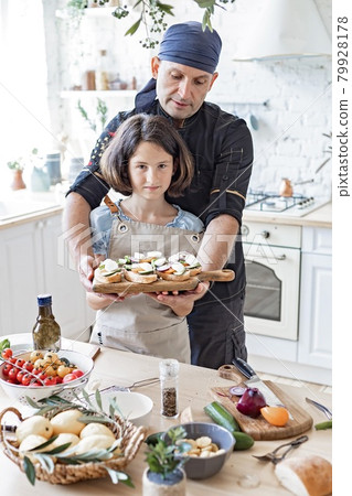 Happy dad chef and his cute daughter are cooking together in the home kitchen. Father and daughter made Italian sandwiches in their home kitchen. Children and parents. Lifestyle photography. Happy dad chef and his cute daughter are cooking together in the home kitchen. Father and daughter made Italian sandwiches in their home kitchen. Children and parents. Lifestyle photography. 79928178
