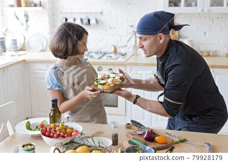 Happy dad chef and his cute daughter are cooking together in the domestic kitchen. Father and daughter are preparing Italian sandwiches in the home kitchen. Children and parents home activities. Happy dad chef and his cute daughter are cooking together in the domestic kitchen. Father and daughter are preparing Italian sandwiches in the home kitchen. Children and parents home activities. 79928179