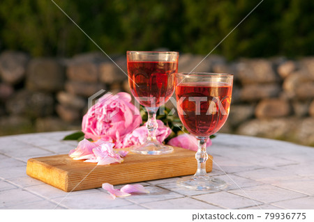 two glasses with rose wine and pink peony bouquet. delicious refreshing drink, huge blossoming flowers at the table two glasses with rose wine and pink peony bouquet. delicious refreshing drink, huge blossoming flowers at the table 79936775