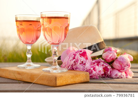 two glasses with rose wine and pink peony bouquet. delicious refreshing drink, huge blossoming flowers and mens hat two glasses with rose wine and pink peony bouquet. delicious refreshing drink, huge blossoming flowers and mens hat 79936781